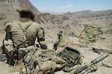 A soldier sits facing a valley in Afghanistan.
