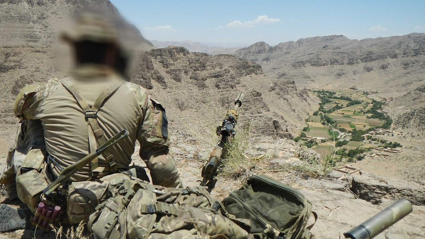 A soldier sits facing a valley in Afghanistan.