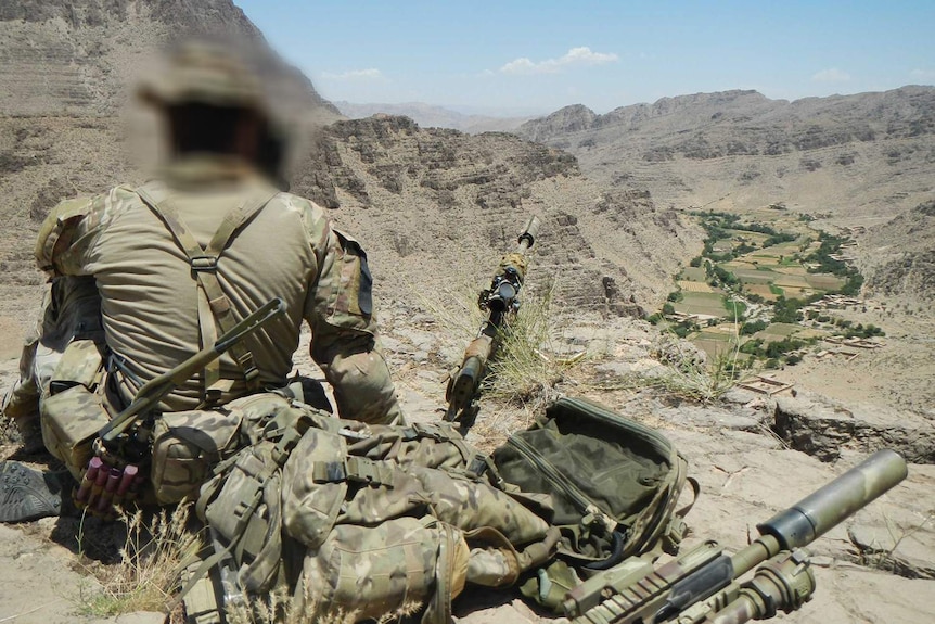 A soldier sits facing a valley in Afghanistan.