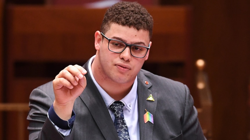 A man wearing glasses sits in a parliament chamber