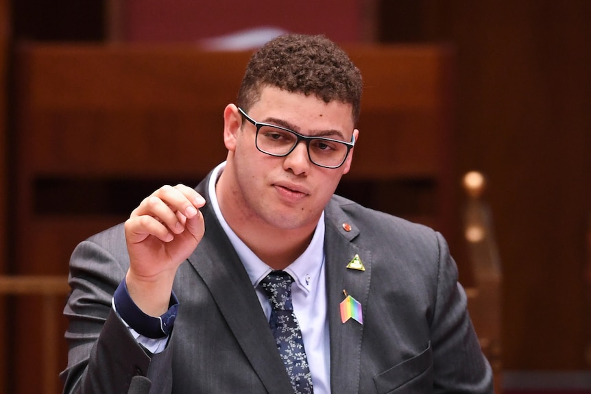 A man wearing glasses sits in a parliament chamber