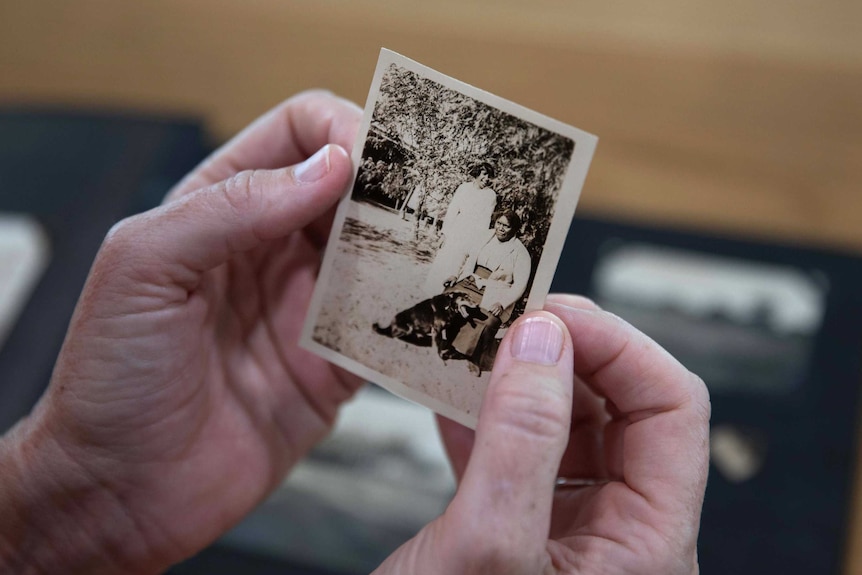 A woman's hands hold a black and white photo of two women