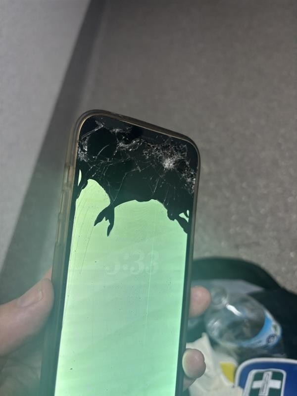 Uma mão segurando um telefone com a metade superior muito danificada.