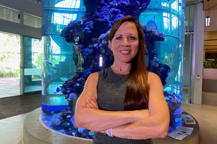A woman stands in an aquarium building with her arms crossed.