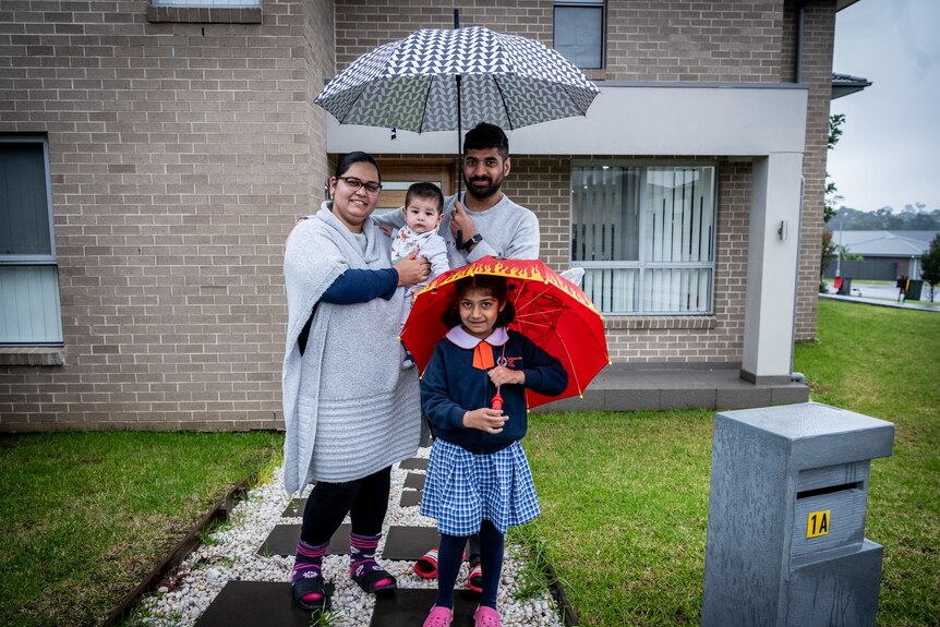 A family holding umbrellas outside a house