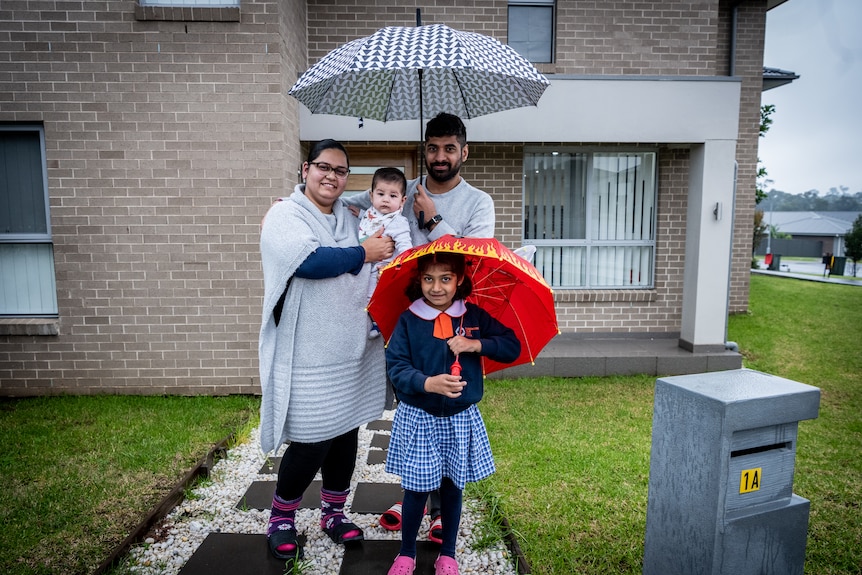 A family holding umbrellas outside a house