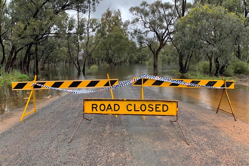 Road closed sign across road in front of flooding and riverside trees