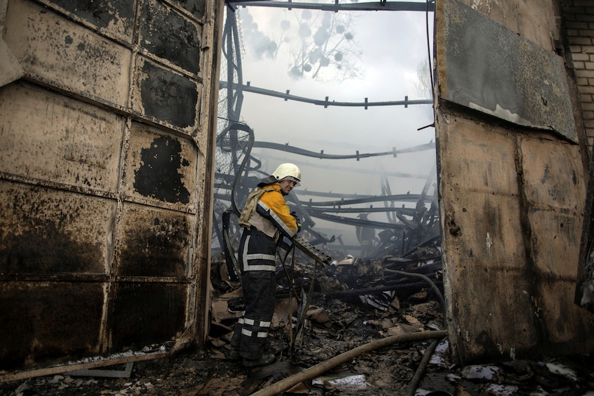 A firefighter stands outside a burnt structure surrounded by smoke.