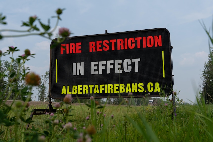 A roadside sign says "Fire restriction in effect. albertafirebans.ca".