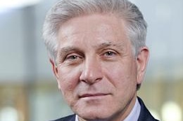 Grey haired man wears blue suit, light blue collared shirt and blue tie with small white spots