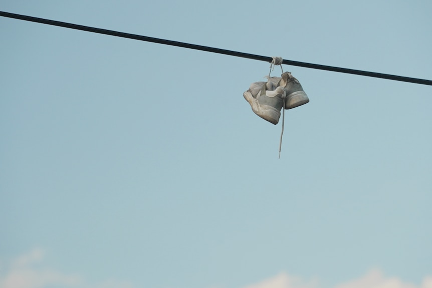 Shoes hang over a power line with blue sky behind