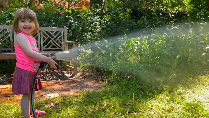 Young girl watering the grass with a hose