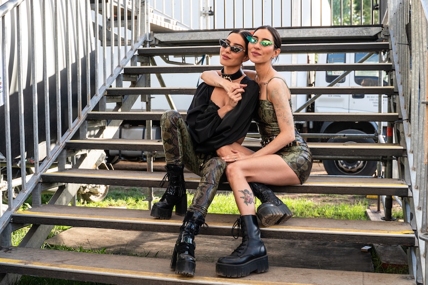 Twin girls in rock outfits pose on demountable stairs backstage at a festival.