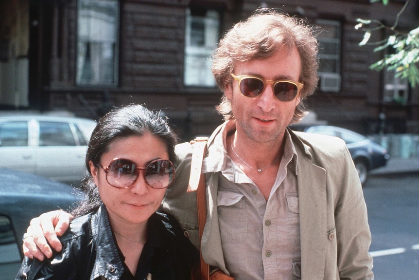 Yoko Ono and John Lennon stand in the street and pose for the camera.