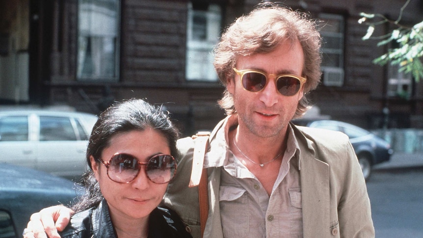 Yoko Ono and John Lennon stand in the street and pose for the camera.