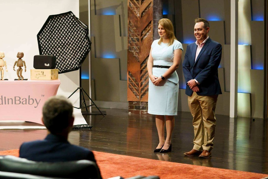 Sandra and Brendon Moffatt standing on the set of Shark Tank with a display of mannequins.