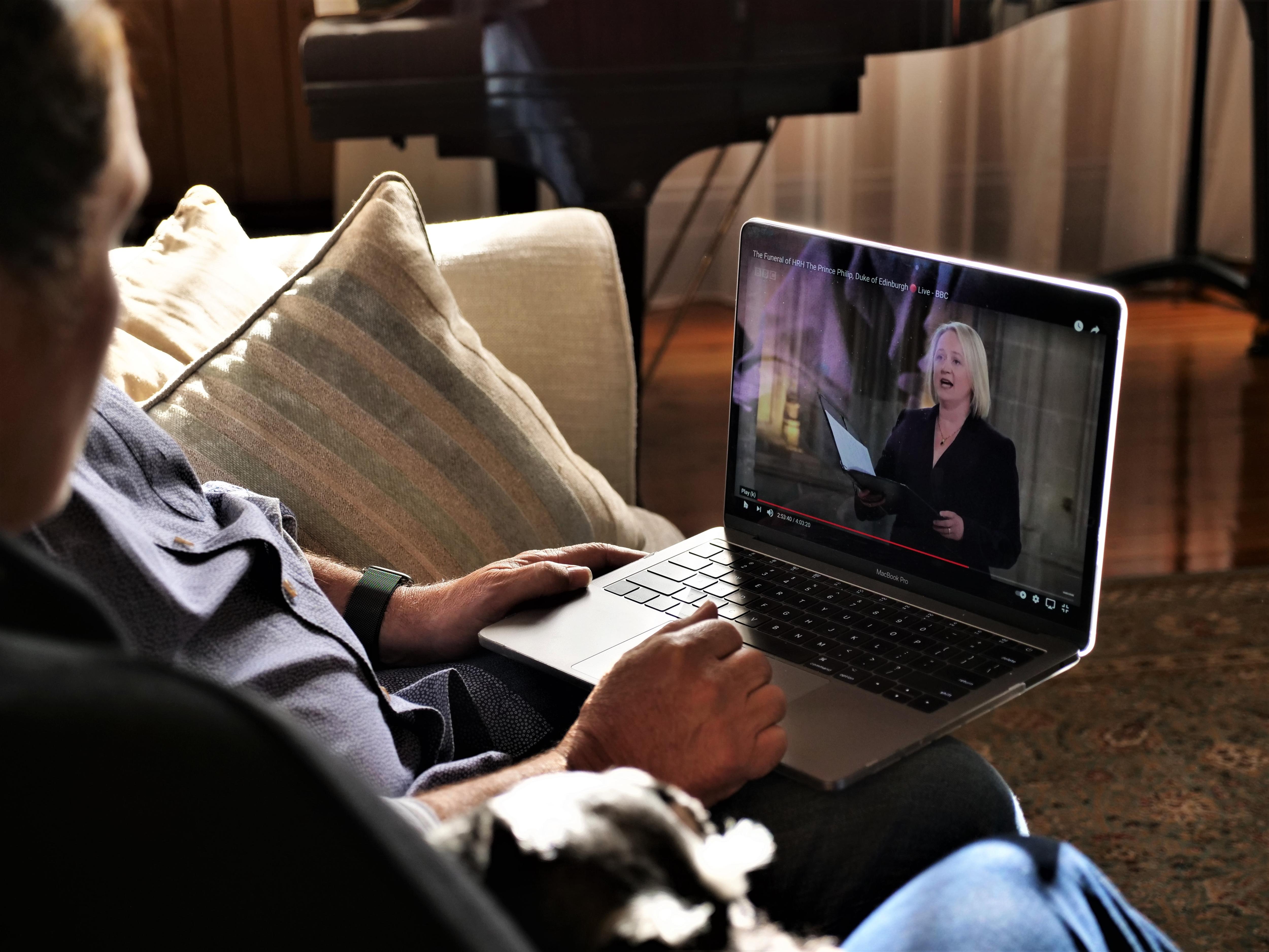 People sit on a couch watching a video on a computer of a woman singing.
