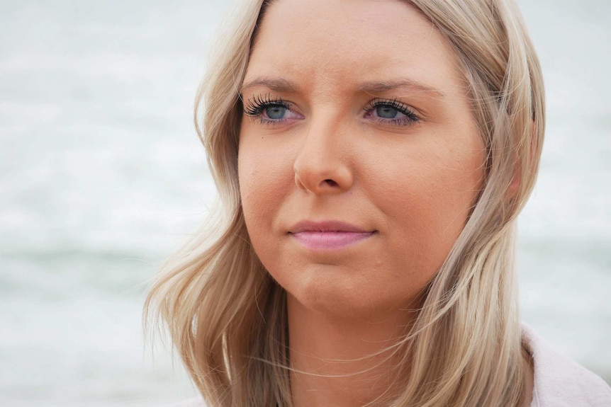 A woman with blonde hair and blue eyes looks solemnly into the distance.