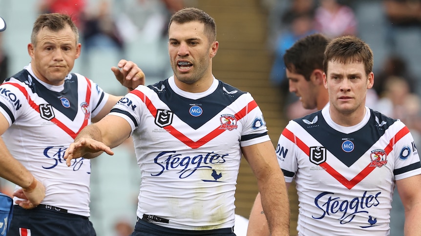 James Tedesco reaches out his hand as he is flanked by Sydney Roosters teammates Brett Morris and Luke Keary.