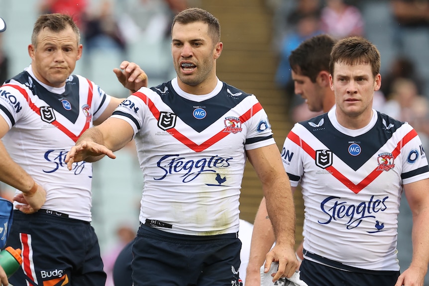 James Tedesco reaches out his hand as he is flanked by Sydney Roosters teammates Brett Morris and Luke Keary.