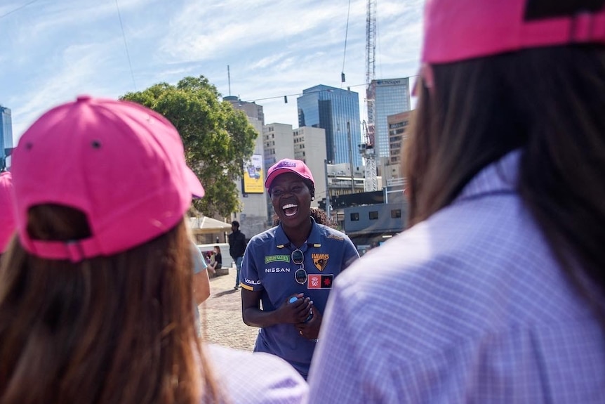 Hawthorn AFLW player Akec Makur Chuot smiling with a group of women surrounding her.