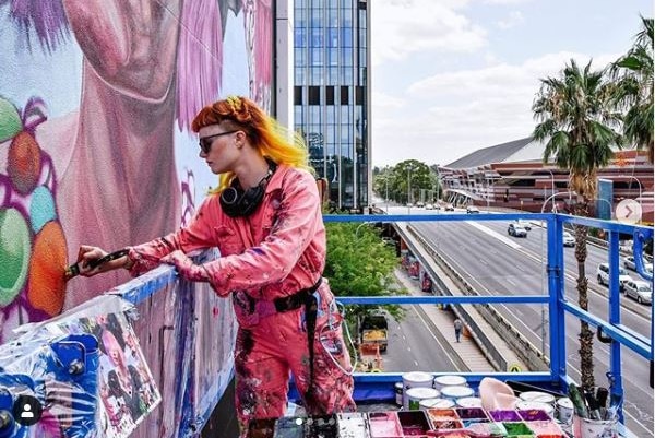 A woman with red hair painting a mural on a wall