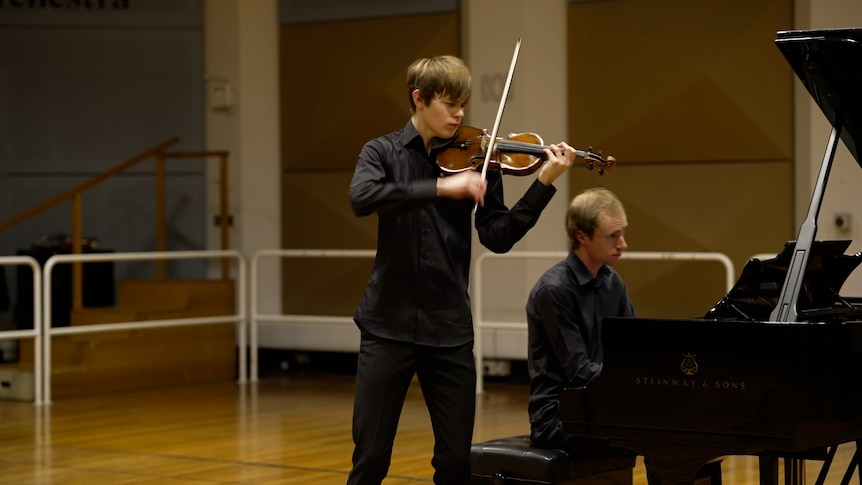 Photograph of a violinist performing in front of a piano.