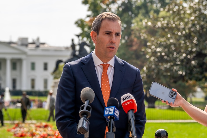 Treasurer Jim Chalmers speaks to media in front of the White House wearing a blue suit and orange tie