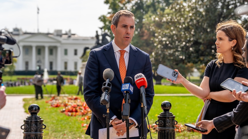 Treasurer Jim Chalmers speaks to media in front of the White House wearing a blue suit and orange tie