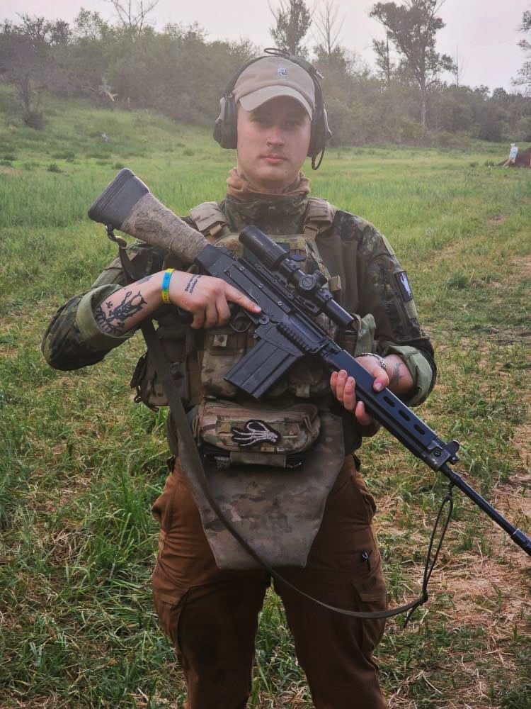 A young man wearing camouflaged clothing and holding a rifle. 