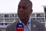 Screenshot of Michael Holding holds a microphone while speaking.