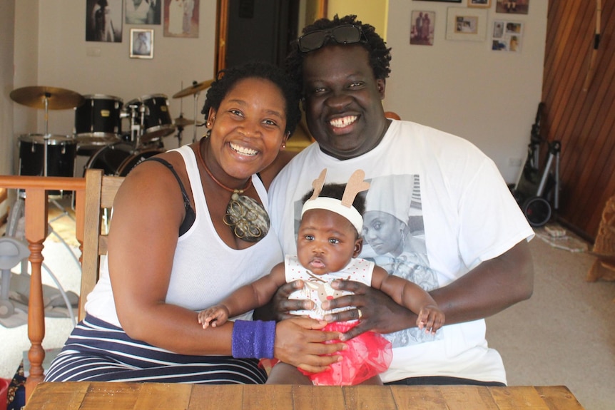 Man and woman with baby girl sitting on their laps, smiling in home setting. 