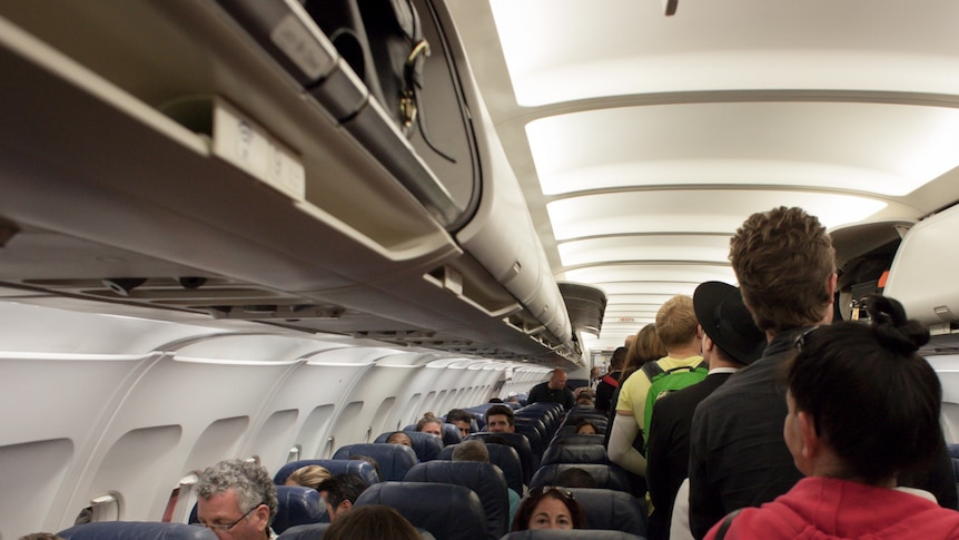 People boarding a plane and putting luggage overhead.