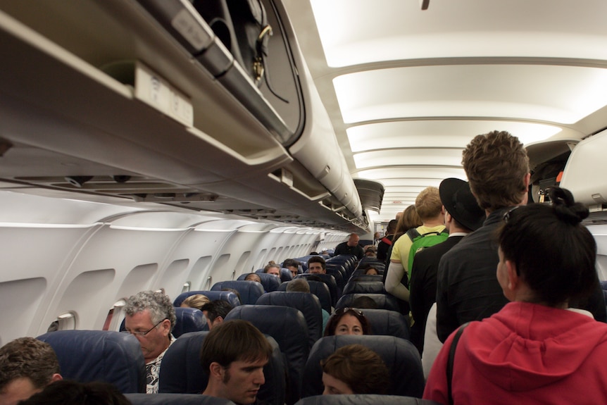 People boarding a plane and putting luggage overhead.