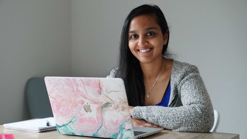 Zoya Patel sitting in front of laptop, smiling.