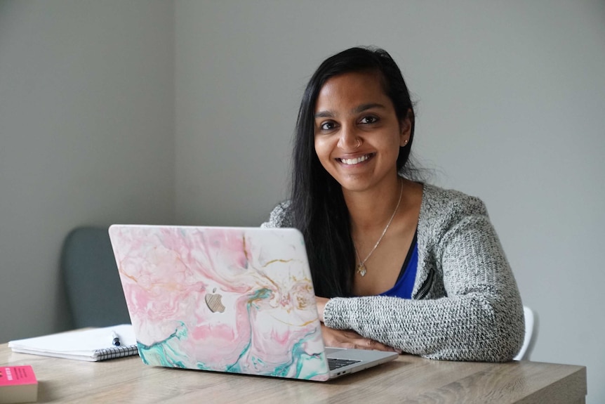 Zoya Patel sitting in front of laptop, smiling.