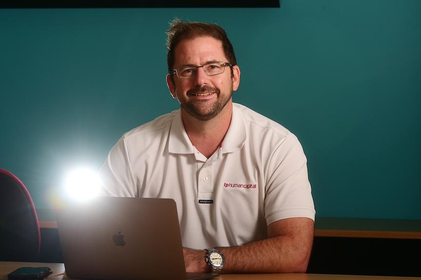 Man in white polo shirt sitting a desk behind his computer