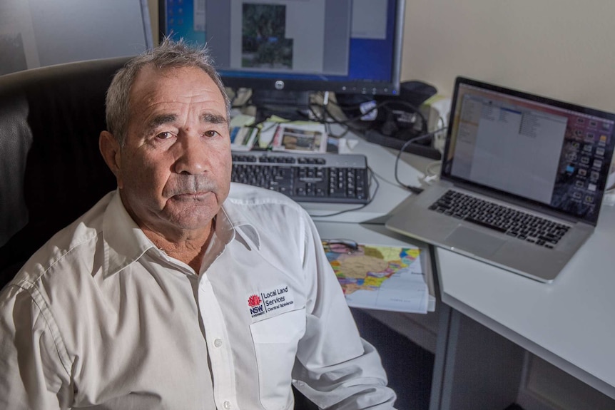 An aboriginal man in a local land services shirt sits in front of maps and computer screens