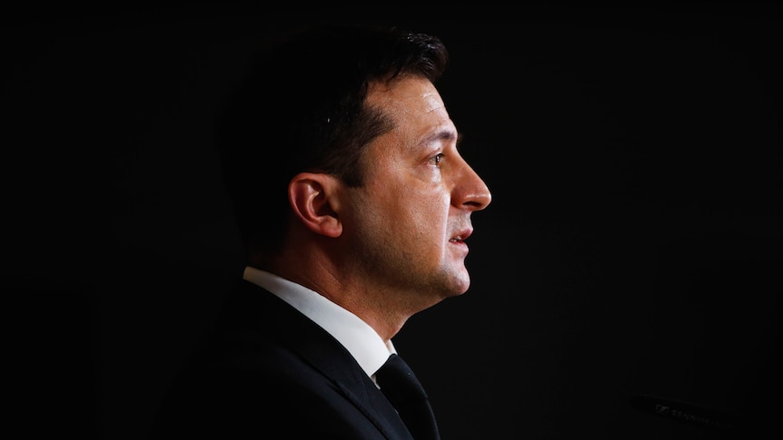 A side angle potrait of Volodymyr Zelenskyy's face with a black background filling the space around him