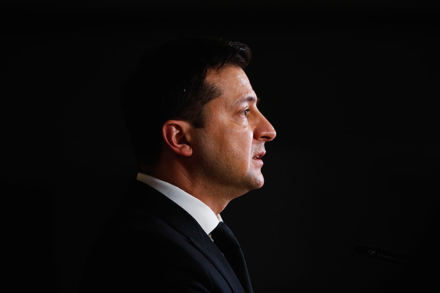 A side angle potrait of Volodymyr Zelenskyy's face with a black background filling the space around him