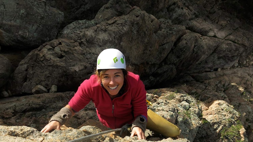 a woman hanging on a rope in front of cliffs