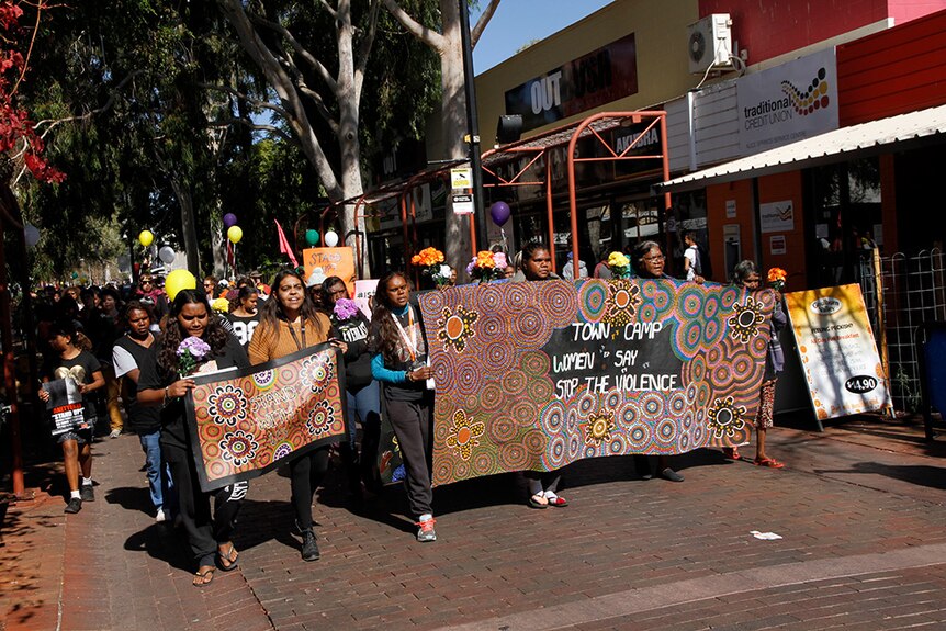 Women marching in central Alice Springs with banners protesting against violence.