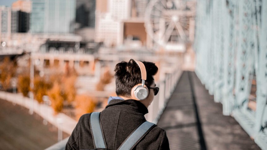 A man wearing a coat listening to headphones and carrying a backpack.