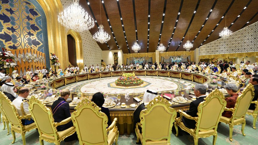Dozens of people sit around a large circular desk in a big room.