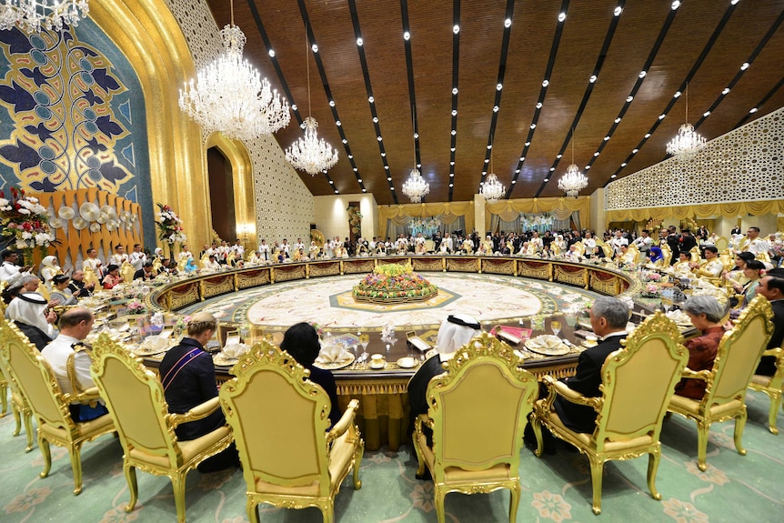 Dozens of people sit around a large circular desk in a big room.