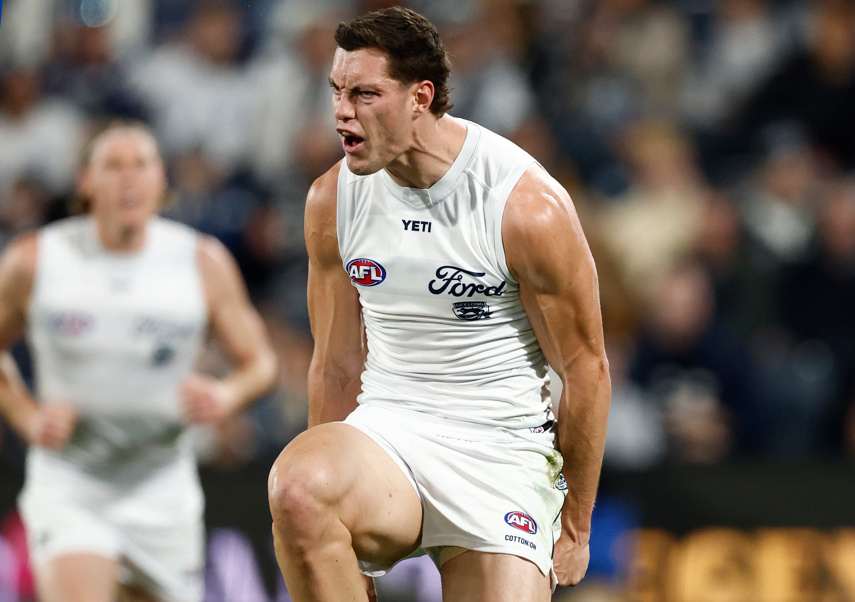 An AFL player in white celebrates a goal by jumping up and down