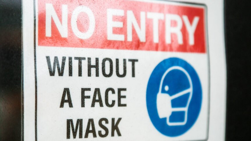Un cartel pegado en una puerta de cristal que dice que no se puede entrar sin mascarilla.