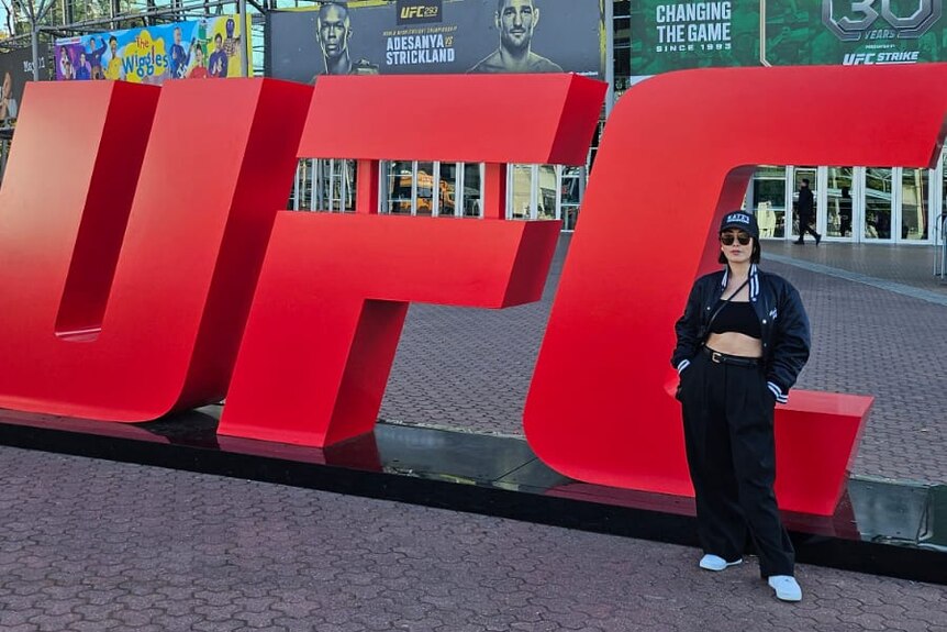 Melissa Leong poses by a huge UFC sign.