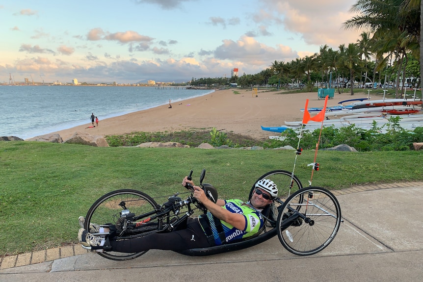 Homme blanc d'âge moyen dans un para-cycle compétitif avec trois roues devant une plage. 