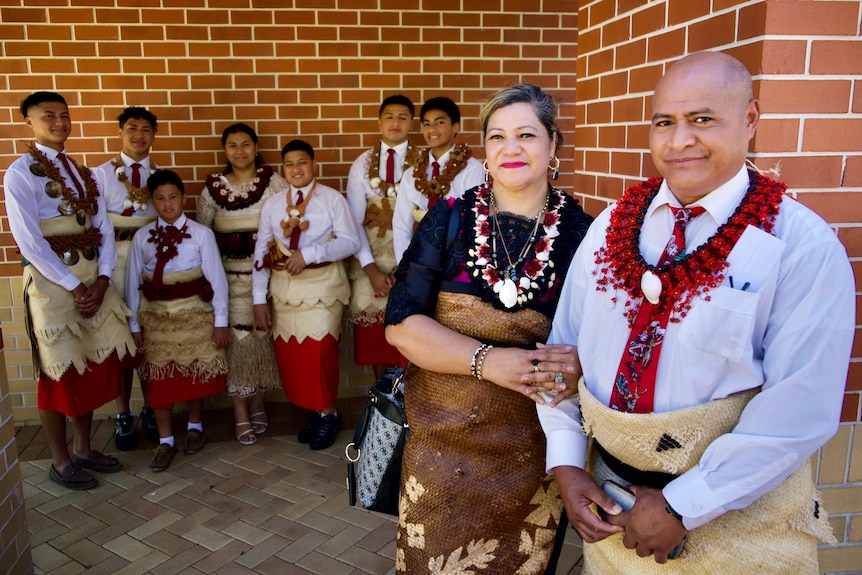 Tevita and Sharon Ta'ai with nine of their children posing in front of a brich wall in traditional Tongan dress.